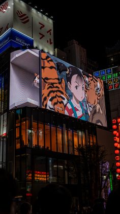 an image of a tiger on the side of a building at night with people walking around