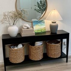 a black table with baskets under a mirror and a lamp on the sideboard next to it