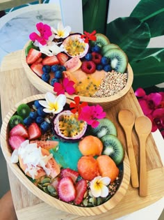 two bowls filled with fruit and flowers on top of a wooden tray next to each other