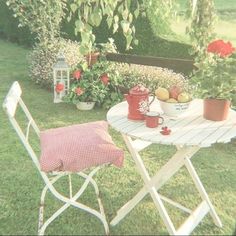 an outdoor table and chair set up in the yard with flowers, fruit and teapots on it