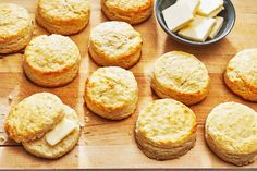 some biscuits and cheese are on a wooden board with a bowl of butter in the background