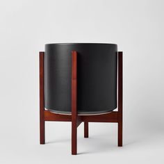 a black leather pot sitting on top of a wooden stand next to a white wall