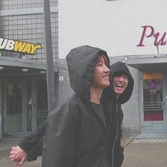 two young men are laughing and walking down the street in front of a pubway