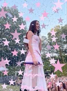 a woman standing on top of a stage in front of pink and white stars with confetti falling from the sky