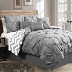 a bed with grey comforter and pillows in a room