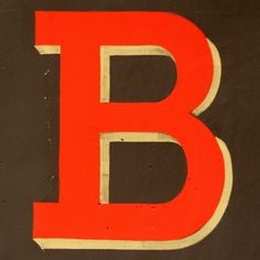 the letter b is painted red and yellow on a brown background with white trimmings