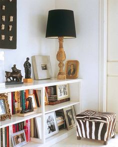 a white book shelf filled with lots of books next to a black and white ottoman