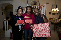 three people are holding presents in front of a christmas tree and posing for the camera