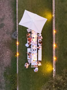 an overhead view of people sitting at a long table with an umbrella over them on the grass