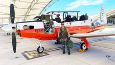 a man standing next to an orange and white airplane