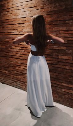 a woman standing in front of a wooden wall wearing a white dress and holding her arms out