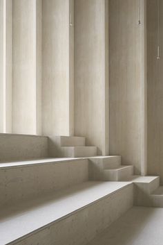 some white steps in an empty room with concrete walls and columns on either side, leading up to the second floor