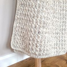 a white crocheted blanket sitting on top of a wooden chair next to a wall