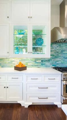 a kitchen with white cabinets and blue glass backsplash