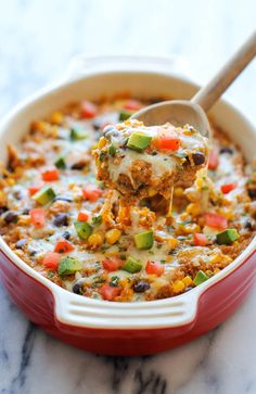 a red casserole dish with a spoon full of mexican chicken enchilade