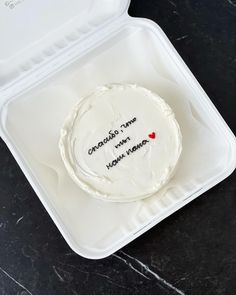 a white cake in a plastic container with writing on the side and a red heart