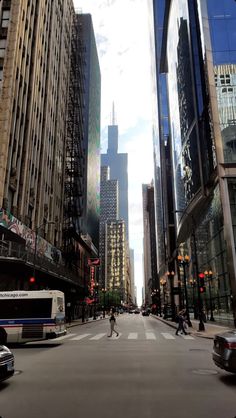 a city street filled with tall buildings next to traffic and people walking on the sidewalk