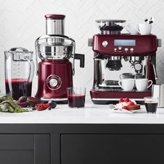 a red coffee maker sitting on top of a counter next to cups and saucers