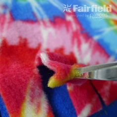 a pair of scissors cutting through the end of a tie - dyed piece of fabric