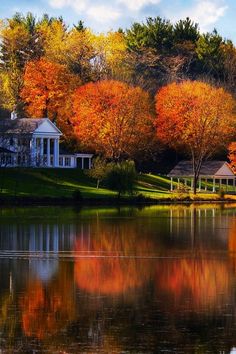 a house on the shore of a lake surrounded by trees with autumn foliage around it