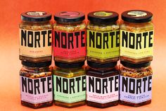 six jars of different types of food sitting on top of an orange surface with the words northnorte written in black