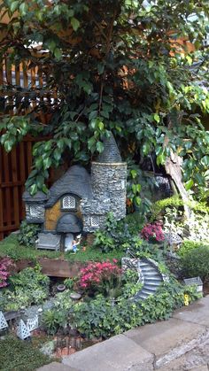 a fairy garden is shown in the middle of some plants and flowers, with stairs leading up to it