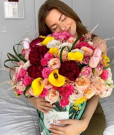 a woman sitting on a bed holding a bouquet of flowers in her hands and smiling at the camera