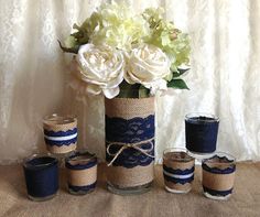 a vase filled with white flowers next to candles and burlock wrapped in twine