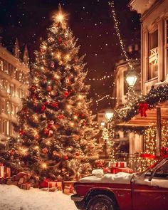 a christmas tree in the middle of a snowy street with lights on it and presents