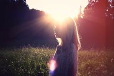 a woman standing in the grass with the sun shining through her hair and looking into the distance