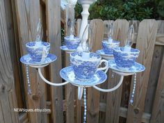 a blue and white candle holder with teacups on it in front of a fence