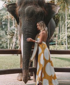 a woman in a yellow and white dress standing next to an elephant