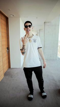 a man in sunglasses and a white shirt making the peace sign with his hand while standing in an empty room