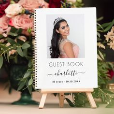 the guest book is placed on an easel next to flowers and greenery, with a portrait of a woman wearing a tiara