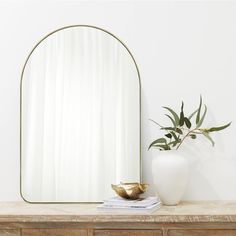 a mirror sitting on top of a wooden dresser next to a vase with a plant in it