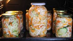 several jars filled with different types of food in an open oven, one containing cucumbers and shredded cheese