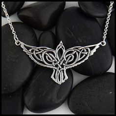 a necklace with an intricate design on it sitting on some black rocks and pebbles in the background