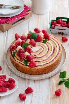 a cake with raspberries on top sitting on a table next to other desserts