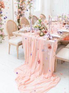 the table is set with pink and purple flowers, candles, and napkins on it