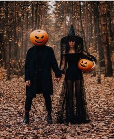 two people dressed up in halloween costumes holding hands and walking through the woods with pumpkins on their heads