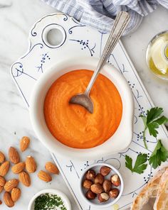 a bowl of carrot hummus with almonds, parsley and bread on the side