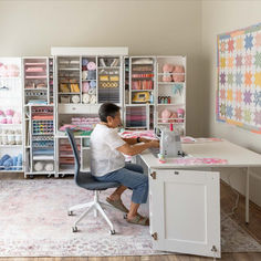 a woman sitting at a sewing machine in front of a table full of craft supplies