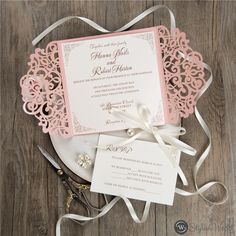 a pink and white wedding stationery on a wooden table with ribbon, scissors and paper