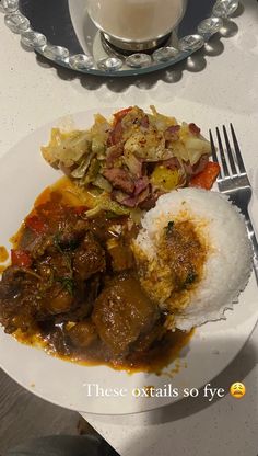 a white plate topped with meat and rice next to a glass of milk on a table