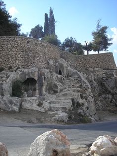 an old stone building sitting on the side of a road next to rocks and trees