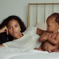 a woman laying in bed with a baby next to her on her chest and arm