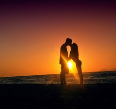 two people kissing on the beach at sunset