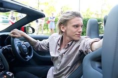 a man sitting in the driver's seat of a car with his hand on the steering wheel