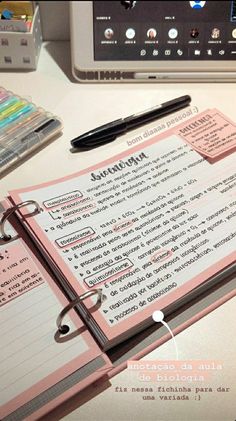 an open notebook sitting on top of a desk next to a pen and laptop computer