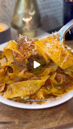 a white plate topped with pasta and meat covered in sauce on top of a wooden table